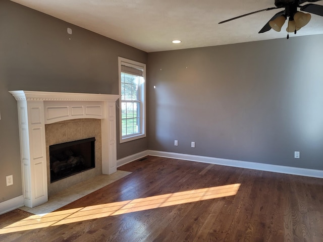 unfurnished living room with ceiling fan, a fireplace, baseboards, and wood finished floors