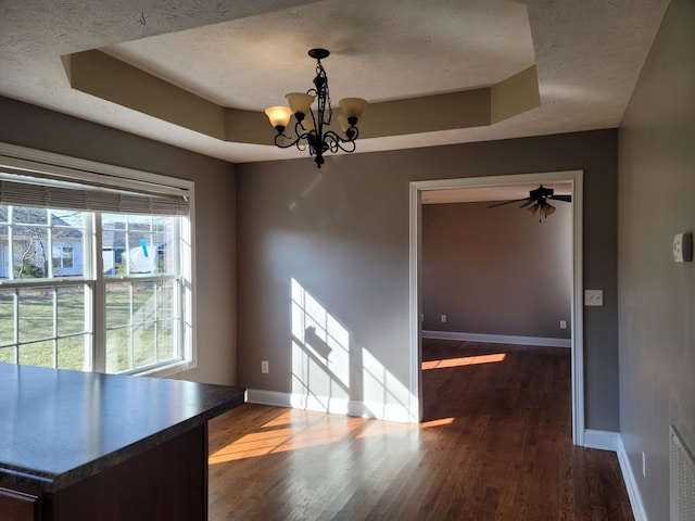 unfurnished dining area featuring a textured ceiling, a raised ceiling, and baseboards