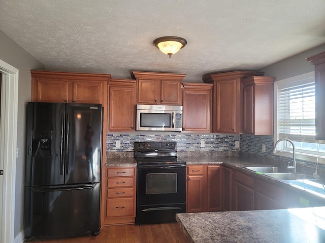 kitchen featuring dark wood-style flooring, dark countertops, backsplash, a sink, and black appliances