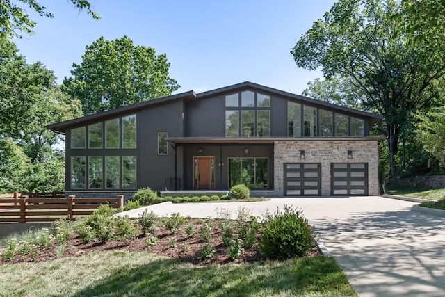 view of front of home featuring a garage, stone siding, driveway, and fence