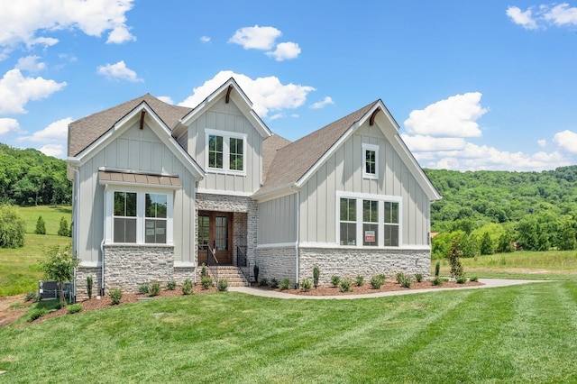 view of front of home featuring stone siding, a front lawn, board and batten siding, and roof with shingles