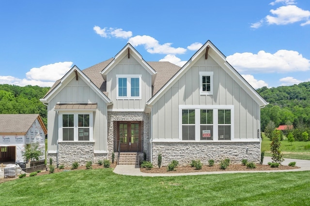 view of front of house featuring stone siding, roof with shingles, board and batten siding, and a front yard