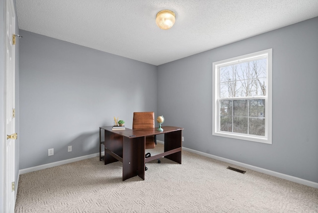 office space featuring baseboards, a textured ceiling, visible vents, and light colored carpet