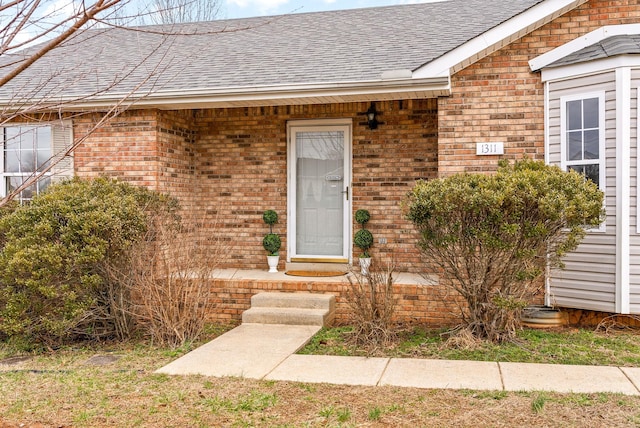 doorway to property with a shingled roof and brick siding