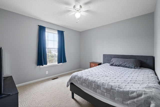 carpeted bedroom with a textured ceiling, a ceiling fan, visible vents, and baseboards