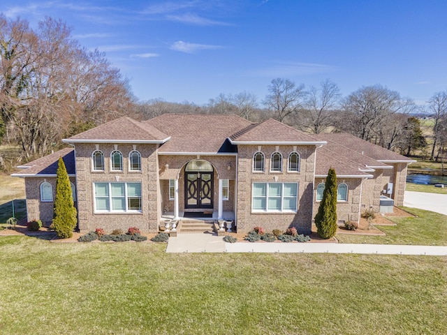 mediterranean / spanish house featuring brick siding, a front lawn, and roof with shingles