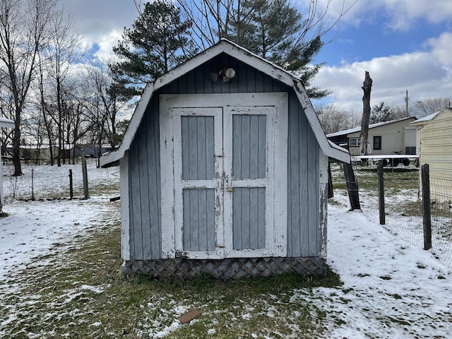 snow covered structure with a storage shed, fence, and an outbuilding