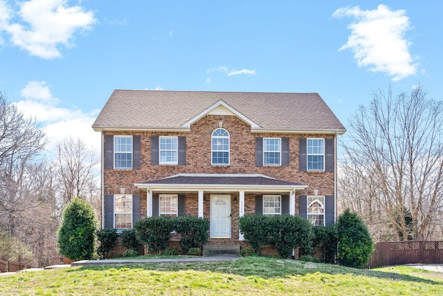 colonial inspired home featuring a front lawn, fence, and brick siding