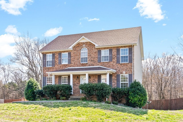 colonial house with brick siding, a front yard, and fence