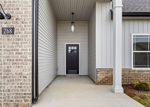 doorway to property featuring brick siding, board and batten siding, and a shingled roof