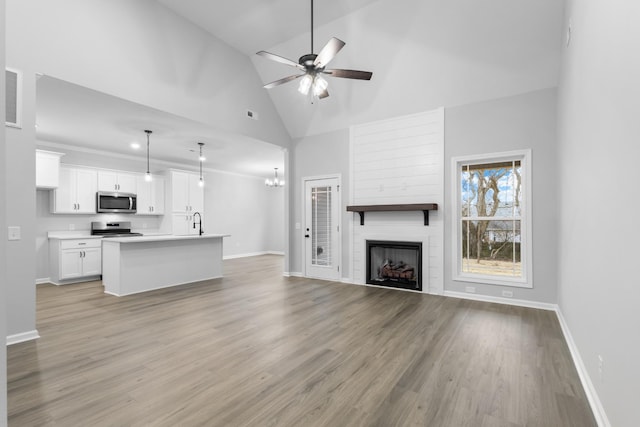 unfurnished living room featuring a large fireplace, high vaulted ceiling, light wood-type flooring, and baseboards