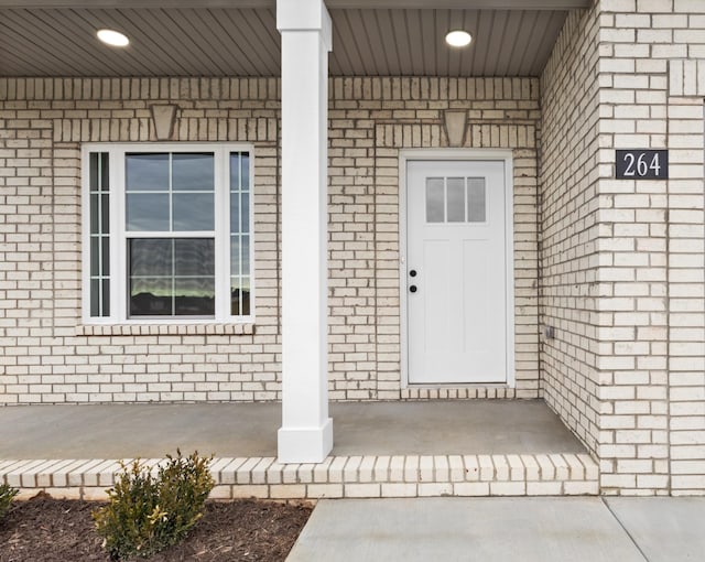 view of exterior entry featuring covered porch and brick siding