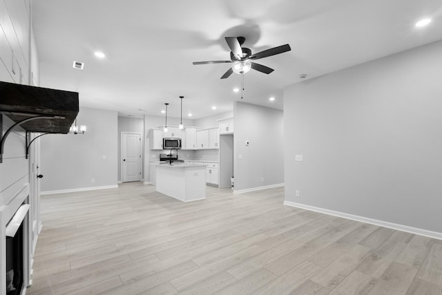 kitchen with stainless steel microwave, open floor plan, a center island, white cabinetry, and pendant lighting