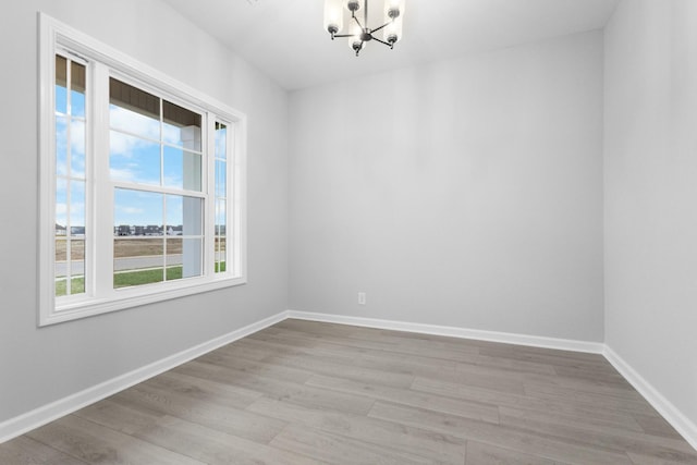 spare room with light wood-style flooring, a chandelier, and baseboards