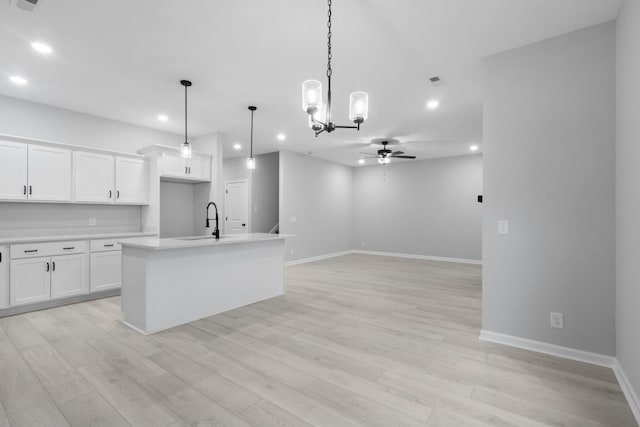 kitchen featuring decorative light fixtures, a center island with sink, light countertops, white cabinets, and a sink