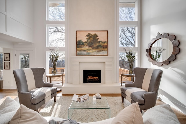 living area with a lit fireplace, a high ceiling, and light wood-style floors