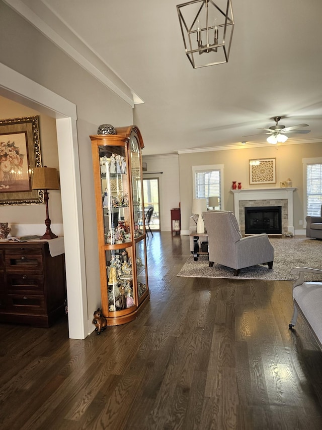 living room featuring ceiling fan with notable chandelier, dark wood-type flooring, a glass covered fireplace, and crown molding