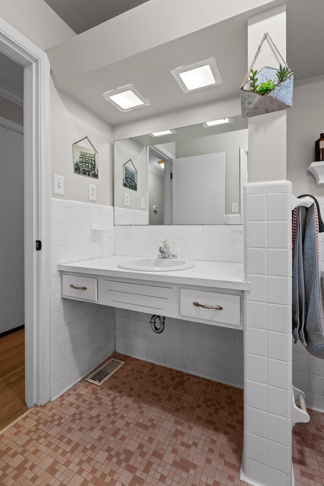 bathroom with a wainscoted wall, visible vents, a sink, and tile walls