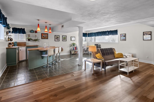 living room featuring dark wood-type flooring, visible vents, decorative columns, and baseboards