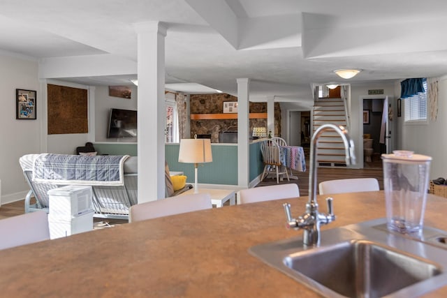 kitchen featuring baseboards, wood finished floors, ornate columns, a fireplace, and a sink