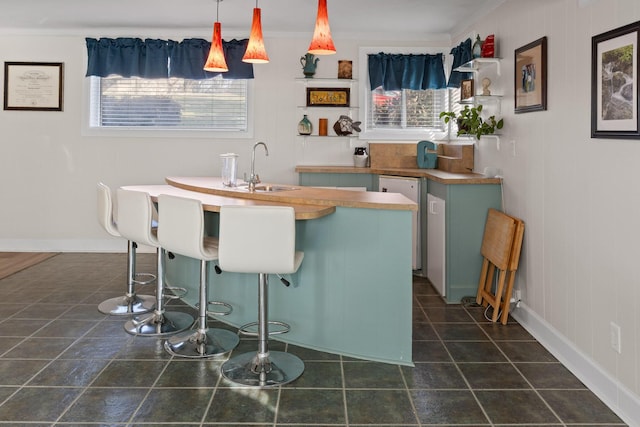 bar with pendant lighting, a sink, dark tile patterned flooring, dishwasher, and baseboards