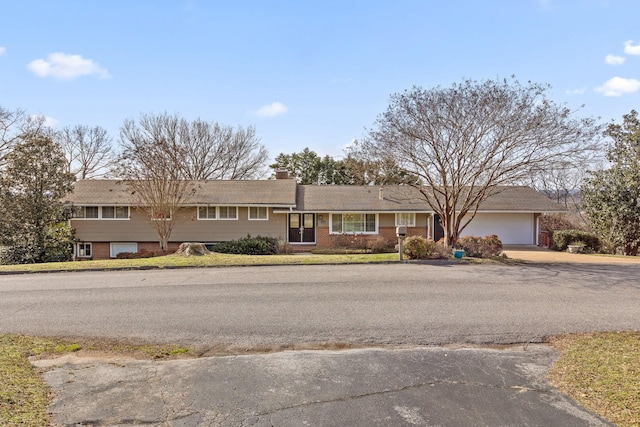 view of front of house with brick siding, driveway, a chimney, and an attached garage