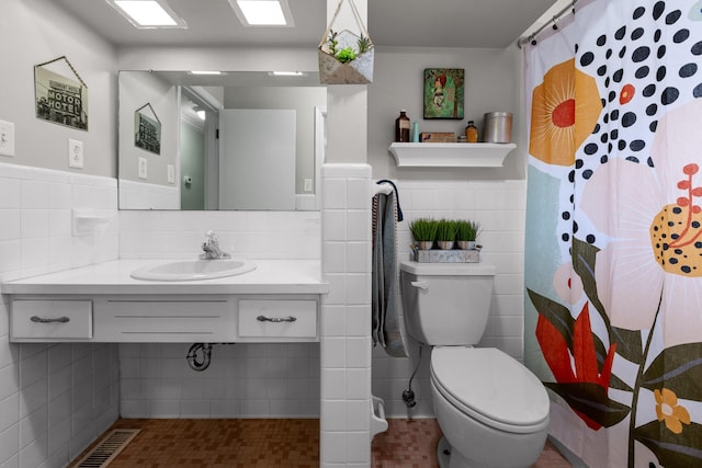 full bath featuring curtained shower, toilet, a sink, tile walls, and wainscoting