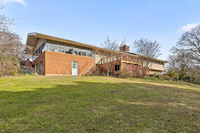 back of house featuring a lawn, a sunroom, a chimney, fence, and brick siding