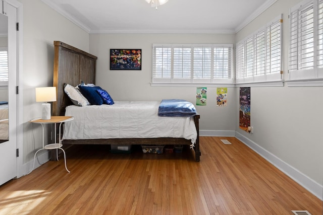 bedroom with visible vents, crown molding, baseboards, and wood finished floors