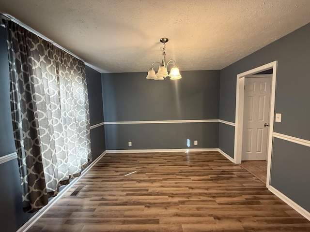 unfurnished dining area with a textured ceiling, dark wood-style flooring, baseboards, and a notable chandelier