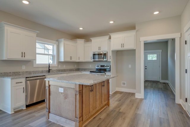 kitchen featuring a kitchen island, light wood-style floors, white cabinets, appliances with stainless steel finishes, and light stone countertops