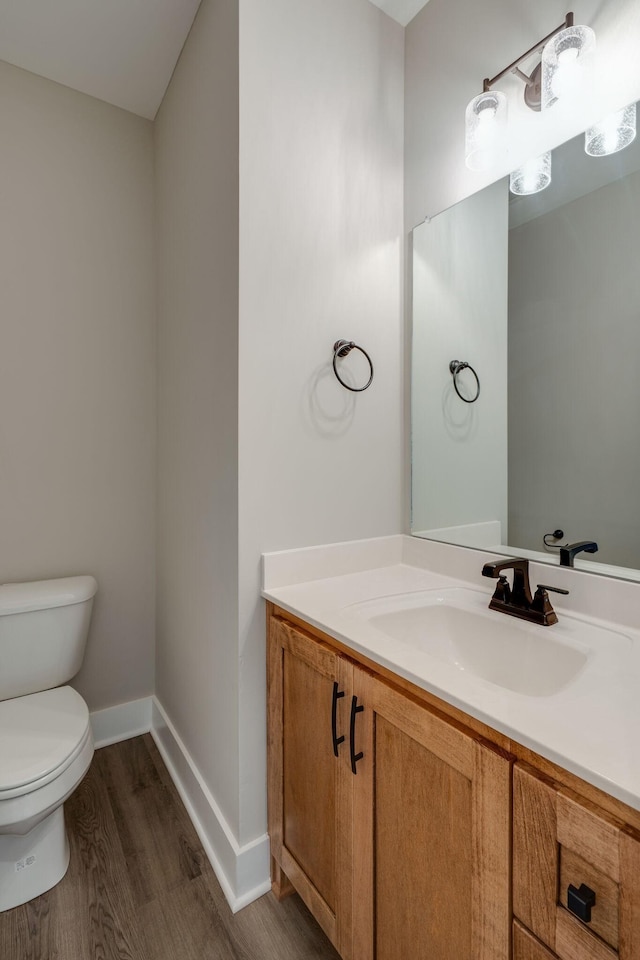 half bath featuring baseboards, vanity, toilet, and wood finished floors