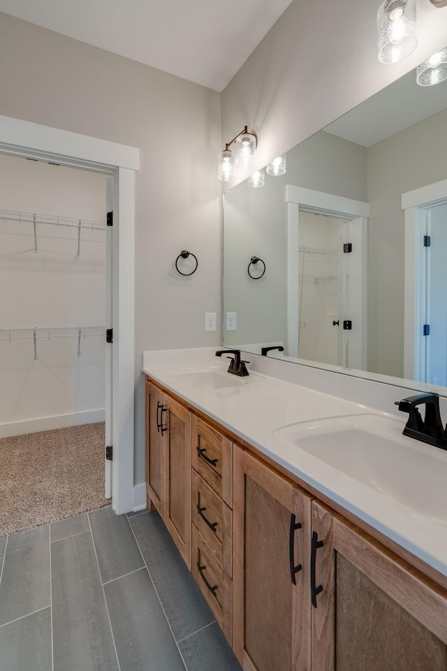 full bath with double vanity, a sink, a walk in closet, and baseboards