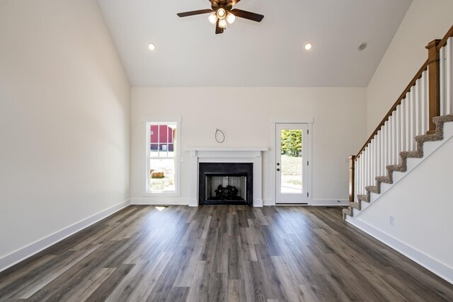 unfurnished living room featuring high vaulted ceiling, dark wood finished floors, stairway, and baseboards