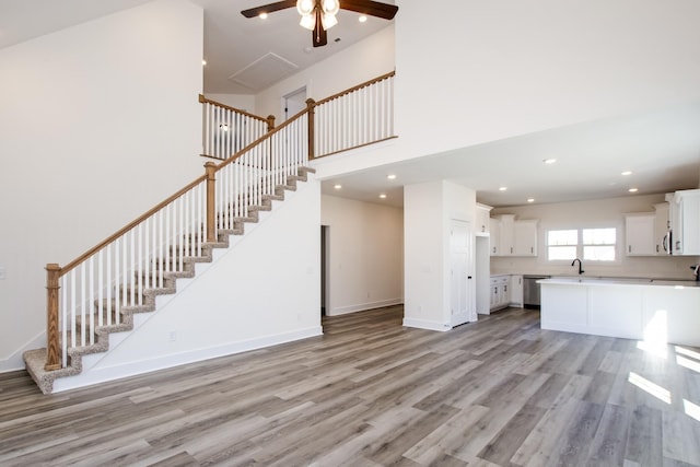 unfurnished living room featuring recessed lighting, a high ceiling, light wood-style floors, a sink, and baseboards