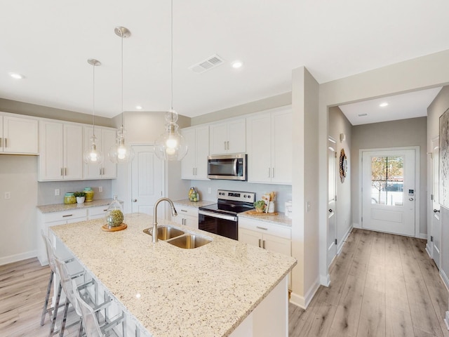 kitchen featuring visible vents, appliances with stainless steel finishes, a kitchen island with sink, pendant lighting, and a sink