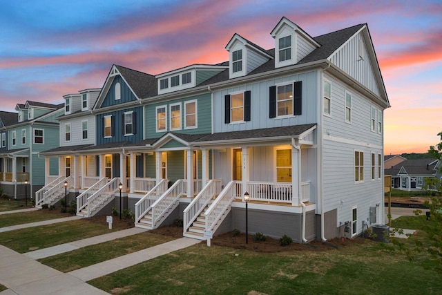 view of property with a yard, a porch, central AC unit, board and batten siding, and stairs