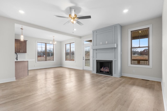 unfurnished living room featuring a fireplace, light wood-style flooring, baseboards, and ceiling fan with notable chandelier