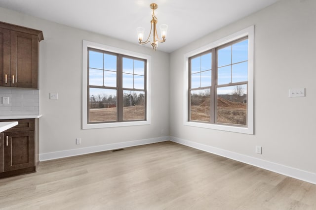 unfurnished dining area featuring light wood-style floors, a chandelier, and baseboards