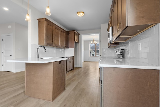 kitchen with light wood finished floors, stainless steel electric stove, light countertops, pendant lighting, and a sink