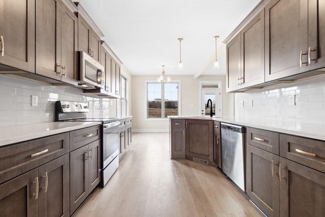 kitchen featuring stainless steel appliances, decorative light fixtures, dark brown cabinetry, and light wood finished floors