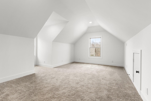 additional living space with light colored carpet, vaulted ceiling, and baseboards