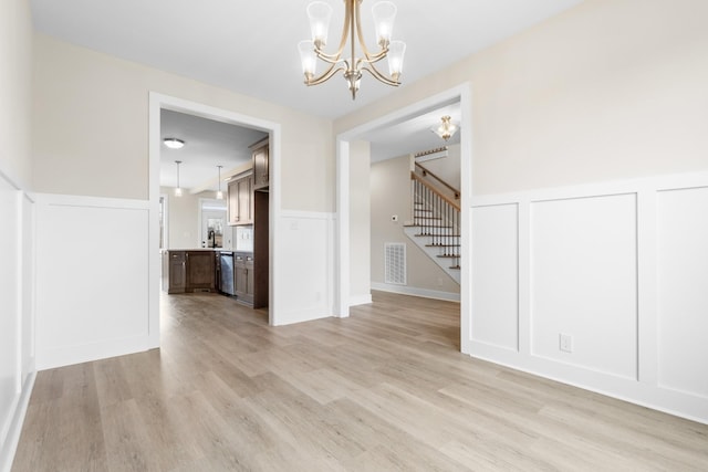 unfurnished dining area with stairs, light wood-style flooring, visible vents, and a decorative wall