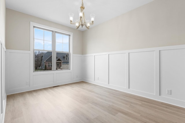 spare room with light wood finished floors, visible vents, a decorative wall, and a notable chandelier