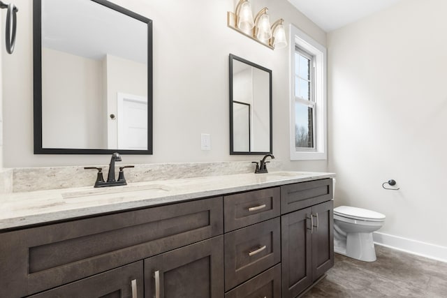 full bathroom featuring double vanity, a sink, toilet, and baseboards