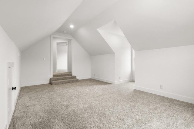 additional living space featuring baseboards, vaulted ceiling, and light colored carpet