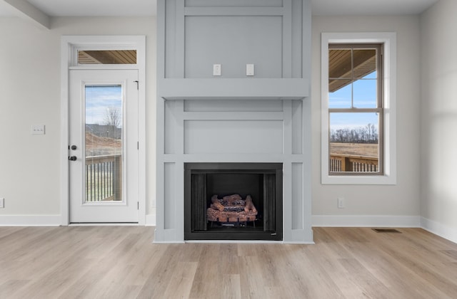 unfurnished living room with a healthy amount of sunlight, a large fireplace, light wood-style flooring, and built in features