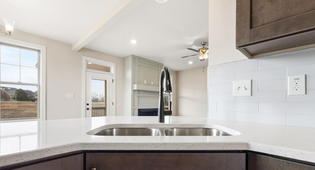 kitchen featuring tasteful backsplash, light stone counters, dark brown cabinets, and a sink