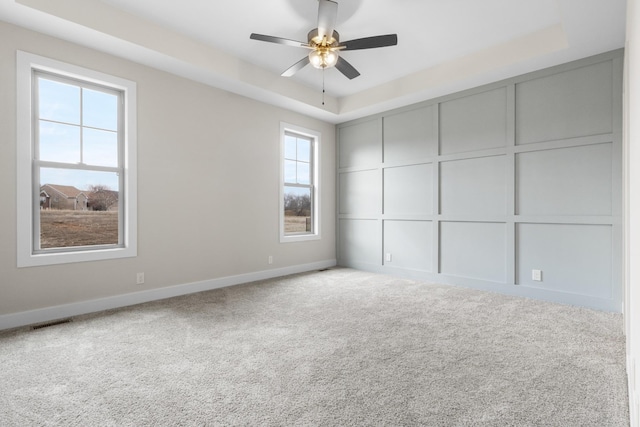 unfurnished bedroom with visible vents, baseboards, a tray ceiling, carpet floors, and a decorative wall