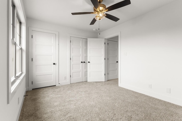 unfurnished bedroom featuring light carpet, multiple closets, a ceiling fan, and baseboards